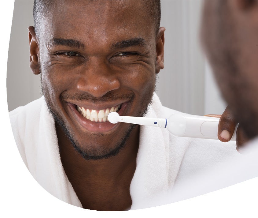 A man smiling while brushing his teeth
